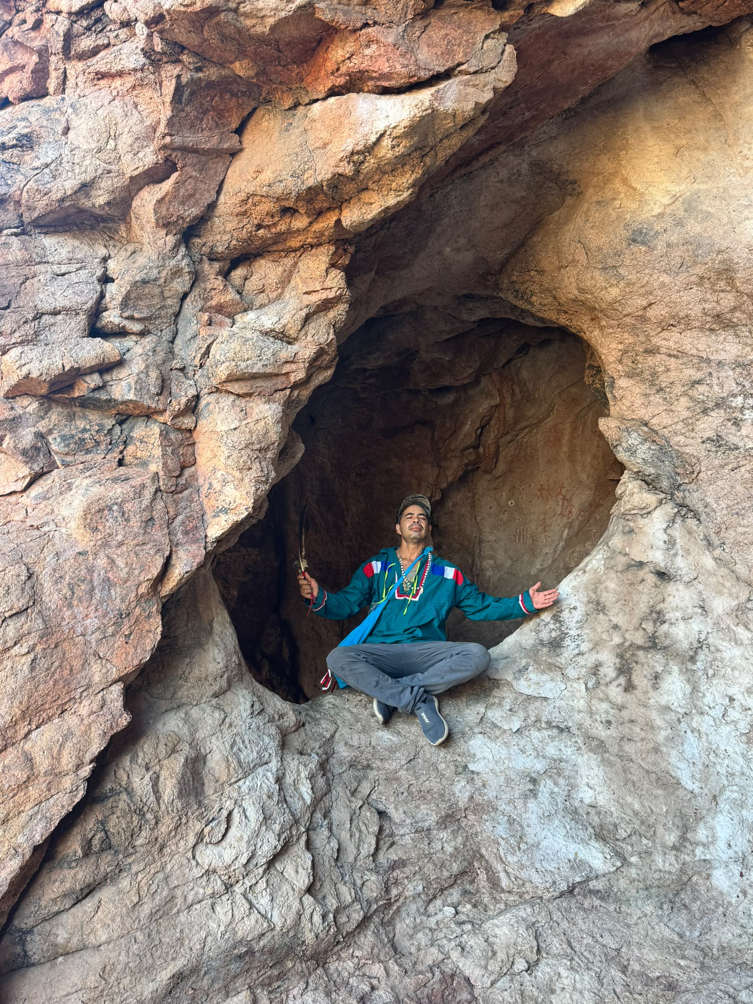 A guardian seated in the mouth of the sacred cave, arms open, in prayer
